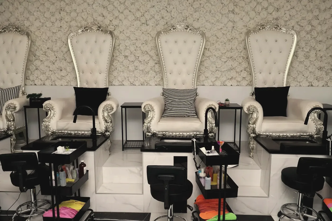 White and silver throne pedicure chairs in front of a white rose wall